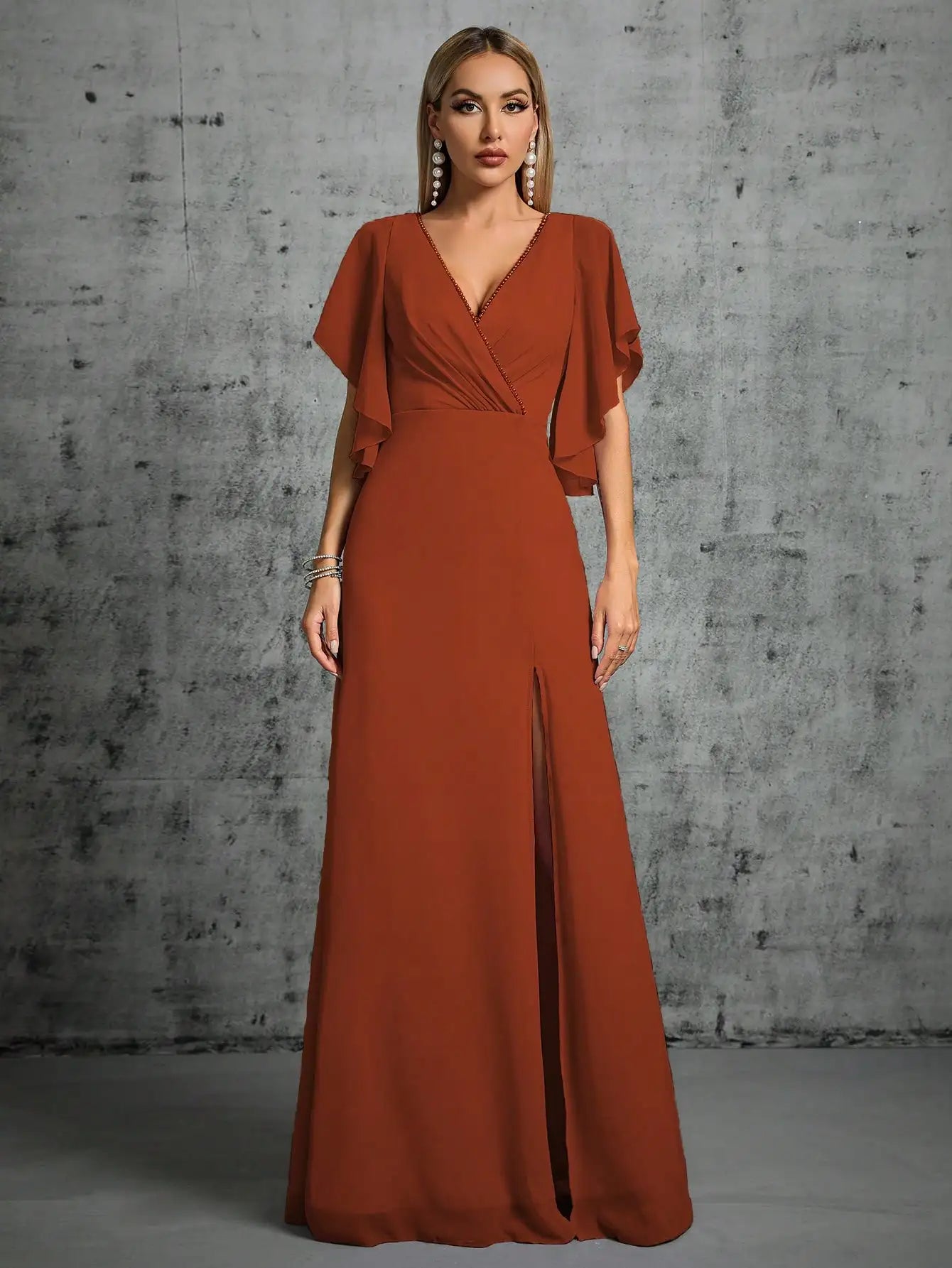 Woman wearing a rust-colored evening gown against a textured gray wall.