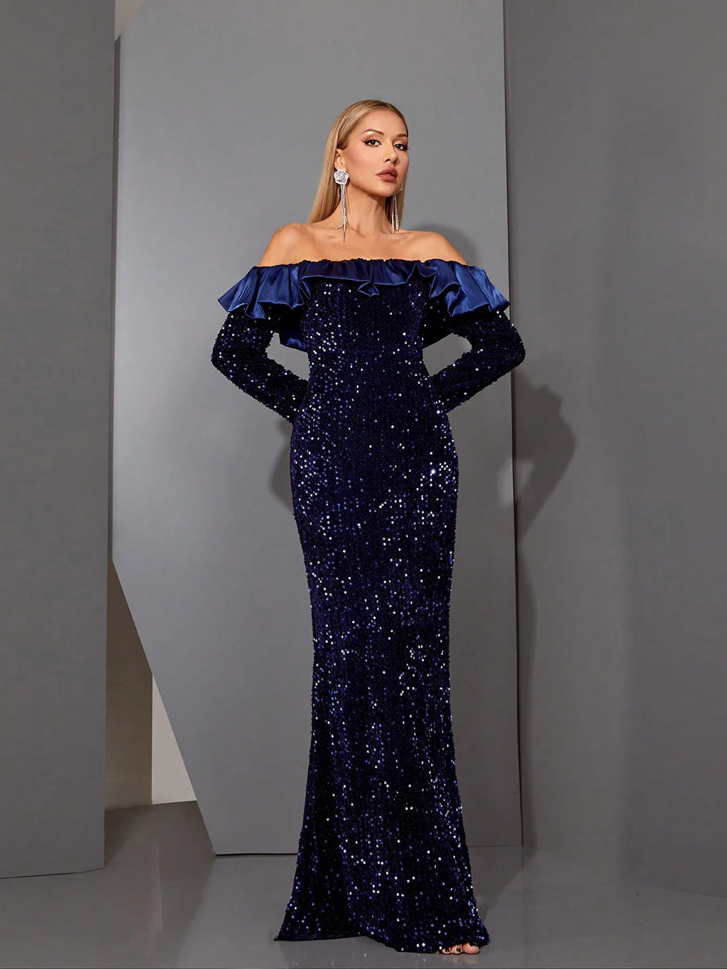 Model posing in navy off-shoulder sequin dress with long sleeves
