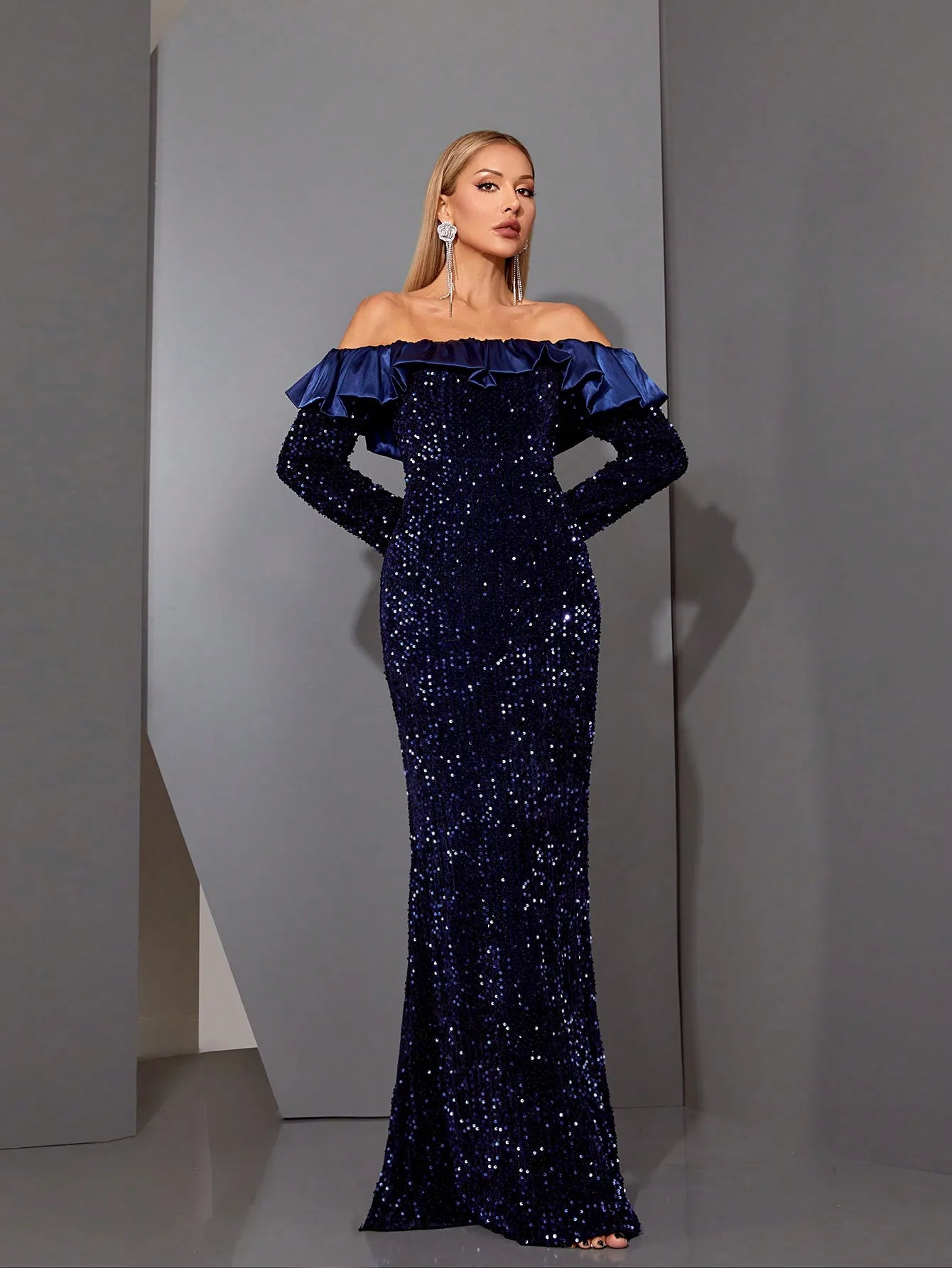 Model posing in navy off-shoulder sequin dress with long sleeves
